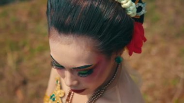 Özenle hazırlanmış makyajlı, göz makyajlı ve kırmızı dudaklı bir sanatçının yakın plan portresi. Denek geleneksel giysiler giyiyor. Renkli süslemelerle süslenmiş, doğal bir arka plana sahip..