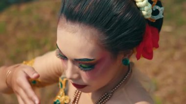 Kayalık arazinin yakınındaki çimenlerde çıplak ayakla yürüyen birinin yakın çekimi. Kişi renkli, desenli bir elbise giyiyor. Hareketle birlikte yavaşça akıyor.