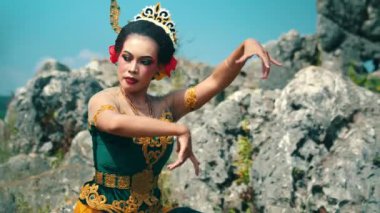 Renkli kostümlü geleneksel bir dansçı, kayalık bir açık havada dans eder. Dansçının özenle hazırlanmış makyaj ve aksesuarları var. Kültürel mirası gözler önüne seriyor. Arka planda doğal kaya oluşumları ve açık mavi bir gökyüzü yer almaktadır..