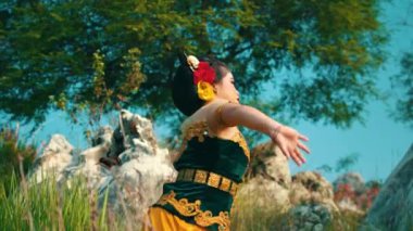 Geleneksel giyinmiş bir dansçı açık havada yemyeşil bir ortamda gösteri yapar.