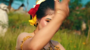 Geleneksel giyinmiş genç bir kadın zarif bir şekilde açık havada poz veriyor, canlı makyaj ve aksesuarlar sergiliyor. Arka planda yeşillik ve açık mavi bir gökyüzü var. Sahnenin kültürel özünü geliştiriyor..