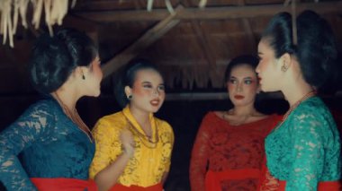 Geleneksel Endonezya kıyafeti giymiş beş kadından oluşan bir grup, kırsal bir ortamda dans ediyorlar. Renkli batik giysiler giyip kuşaklar takıyorlar. Kültür mirası sergiliyorlar..