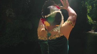 Geleneksel giyinmiş, çiçek desenli, kollarını açmış yeşil ve güneş ışığına karşı koyan bir dansçı..