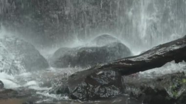 Kayaların üzerinde çağlayan bir şelalenin yakın çekim görüntüsü, sıçramalar ve sis yaratıyor. Sahne, suyun dinamik hareketini ve ıslak taşların dokusunu yakalar..