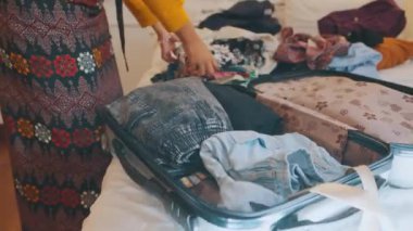 Bayan bir gezgin eşyalarını düzenliyor, desenli gömlekleri ve kotu açık bir bavula koyup yatağa katlıyor. Yaklaşan yolculuk için hazırlık.