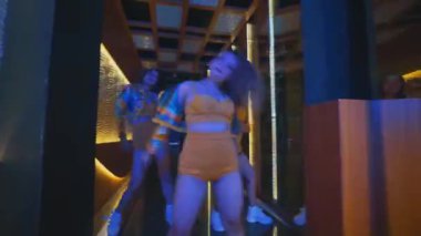 Üç dansçı, aynalı koridorda iki parçalı sarı kıyafetler ve ceketler giyerek hip hop hareketleri yapıyor..