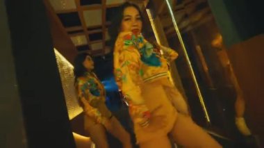 Üç dansçının, sarı şehir kıyafetleri içinde, aynalı koridorda senkronize hip-hop hareketleri yaparken çekilmiş, dinamik, alçak açılı bir çekim..