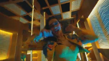 Şen şakrak bir bayan dansçı lüks bir koridorda dönüyor ve sarı bir elbise ve ceket içinde gülüyor..