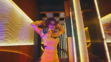 Dar, aydınlık bir koridorda müzik eşliğinde dans eden profesyonel bir dansçının tüm vücut pozu. Sahnede sıcak ortam ışıkları ve modern mimari ayrıntılar yer alıyor..