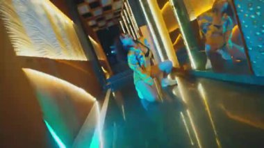 Yetenekli bir dansçı, neon ışıklı bir tünelde yer döşemesi ve diz çökme hareketleri yapar. Sarı kostümlü, kulüp ortamında genç bir Asyalı kadının dinamik performansı..