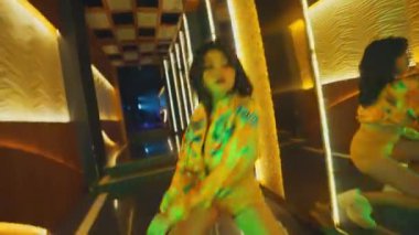 Karaoke ya da otel koridorunda ritmik dans eden bir kızın yan görüntüsü. Kalçalarını ve adımlarını ritme göre hareket ettiriyor. Işıklar ve aynalarla aydınlatılıyor..