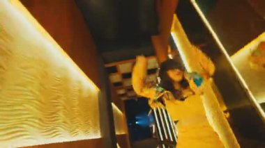 Genç bir kadın, altın bir koridorda şehvetli ve yavaş bir dans gösterisi yapıyor. Gece mekanında büyüleyici bir atmosfer yaratmak için el hareketlerini ve vücut hareketlerini kullanıyor..