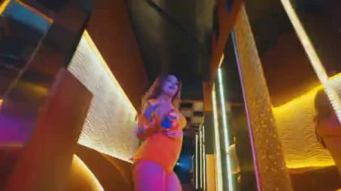 Bir bayan dansçı, aynalı koridorda kameraya doğru güvenle yürür ve sarı şehir kıyafetini giyer..