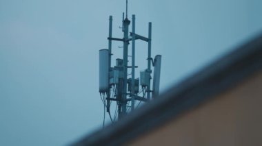 Mavi gökyüzüne karşı bir telekomünikasyon kulesinin yakın görüntüsü. Kulede modern iletişim teknolojisi sergilenen birden fazla anten ve ekipman bulunuyor..
