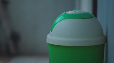 Yuvarlak bir kapağı ve pürüzsüz bir yüzeyi olan yeşil ve beyaz bir çöp tenekesinin yakın çekimi. Arkaplan bulanık, çöp kutusunun tasarımını vurguluyor.