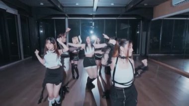 Bir grup dansçı geniş pencereli geniş bir stüdyoda koreografi gösterisi yapıyorlar. Dansçılar şık kıyafetler giyiyorlar, siyah beyaz kıyafetler sergiliyorlar. Işıklandırma dramatik, hareketlerini vurguluyor..