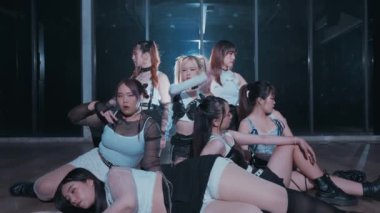 Bir dans stüdyosunda çarpıcı şekilde poz veren yedi dansçıdan oluşan bir grup. Şık, hareketli kıyafetler giyiyorlar, dans stillerinin karışımını sergiliyorlar. Işık dengesiz bir atmosfer yaratıyor, pozlarını ve ifadelerini vurguluyor..