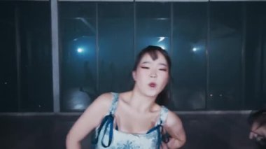 Dinamik bir dans gösterisi. Dört kadın şık kıyafetler içinde loş bir stüdyoda enerjik hareketler sergiliyor. Mavi ışıklandırma ve modern estetik ile atmosfer canlı..