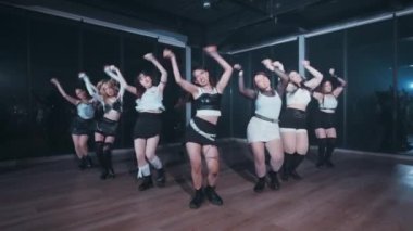 Altı dansçıdan oluşan bir grup bir dans stüdyosunda senkronize bir gösteri yapıyor. Şık, hareketli kıyafetler giyiyorlar, dinamik hareketler sergiliyorlar. Stüdyonun loş ışıklı geniş pencereleri var, dramatik bir atmosfer yaratıyor..