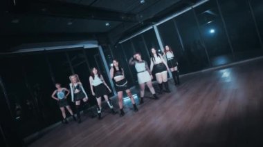 Bir grup dansçı loş bir stüdyoda koreografi gösterisi yapıyor. Dansçılar şık kıyafetler giyiyorlar ve çeşitli dinamik pozlar veriyorlar. Enerjilerini ve senkronizasyonlarını sergiliyorlar..