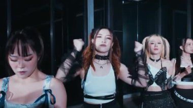 Bir grup genç kadın loş bir şehir ortamında dans gösterisi yapıyor. Şık ve şık kıyafetler giyiyorlar. Renk ve dokuların karışımını sergiliyorlar. Atmosfer enerjik ve canlı, bir dans gösterisinin özünü yakalıyor..