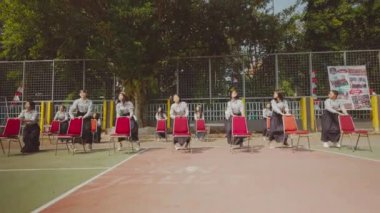 Açık hava basketbol sahasında arka planda çitleri ve ağaçları olan bir grup boş kırmızı sandalye..