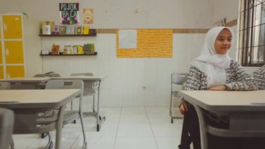 Sınıfta oturmuş gülümseyen ve kameraya bakan bir grup öğrenci. Sınıfın sarı dolapları ve biraz süslemeli beyaz duvarları var..