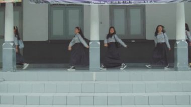 Bir grup üniformalı kız, elinde sütunlarla bir binanın önünde yürüyor..