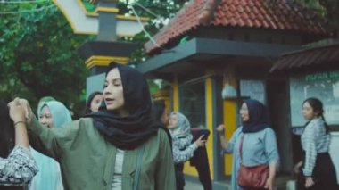 Bir grup kadın, bazıları başörtüsü takıyor, dışarıda duruyorlar. Görüntü biraz bulanık, samimi ve spontane bir his veriyor..