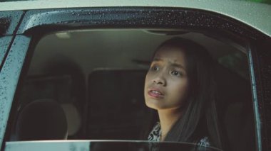 Yağmurlu bir günde araba camından dışarı bakan genç bir kız.