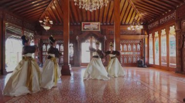 Güzel dekore edilmiş ahşap bir salonda geleneksel bir dans gösterisi. Akan etekli zarif kostümlü dansçılar, kültür mirasını sergiliyorlar. İç kısımda karmaşık oymalar ve avize var..