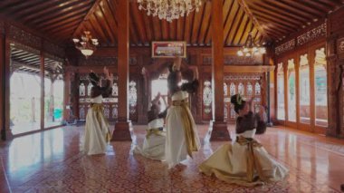 Dört dansçıdan oluşan bir grup, güzel dekore edilmiş ahşap bir salonda geleneksel giysiler içinde, karmaşık oymalar ve bir avize ile gösteri yapıyorlar..