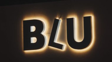 'BLU' harflerinin yer aldığı ışıklı bir tabelanın yakın çekimi. Harfler kalın ve modern, çevrelerinde yumuşak bir parıltı var, koyu bir arkaplan üzerine kurulmuş..