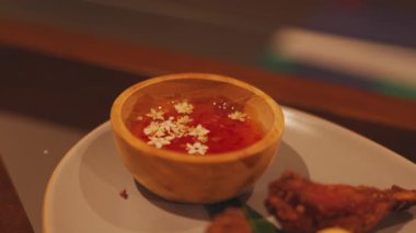 Küçük beyaz çiçeklerle süslenmiş, kızarmış tavuk kanatlarıyla bir tabağa yerleştirilmiş, tatlı sosla dolu ahşap bir kase..