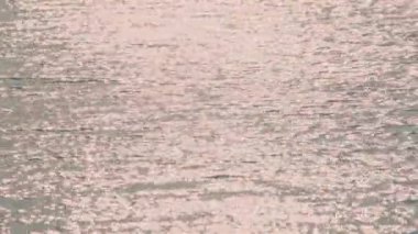 Suyun yumuşak pembe renkleri yansıtan sakin bir görüntüsü, sakin ve rüya gibi bir atmosfer yaratıyor. Yüzey ışıkla parıldıyor, sükunet hissi uyandırıyor..