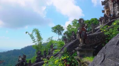 Yamaçtaki bir tapınak kompleksinin manzarası. Karmaşık taş heykeller ve gür yeşillikler. Gökyüzü parçalı bulutlu, sakin atmosferi güçlendiriyor..