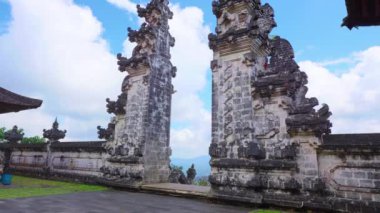 Endonezya, Bali 'deki bir tapınağın antik taş kapılarının manzarası, yemyeşil ve bulutlu mavi gökyüzü ile çevrili..