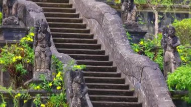 Her iki taraftaki karmaşık heykellerle süslenmiş, yemyeşil bir merdiven manzarası. Merdiven, geleneksel Bali mimarisini gözler önüne seren sakin bir manzaraya çıkıyor..