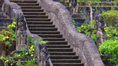 Her iki tarafta karmaşık heykellerle süslenmiş taş merdivenlerin manzarası, yemyeşil ve canlı çiçeklerle çevrili, dingin ve mistik bir atmosfer yaratıyor..
