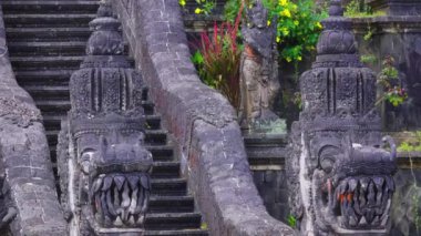 Efsanevi yaratıkların karmaşık taş oymaları yemyeşil yeşilliklerle çevrili bir dizi antik merdiveni kuşatır. Yıpranmış taş, geleneksel Balili sanatını sergileyen ayrıntılı doku ve ifadelere sahip..