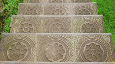 Yeşil çimlerle çevrili, karmaşık çiçek desenli dekoratif taş basamakların yakın görüntüsü..