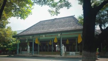 Ağaçlarla çevrili fayanslı çatılı geleneksel bir bina. Yapıda saçaklardan sarkan büyük sarı süslemeler ve civarda heykeller ve yeşillikler yer alıyor..