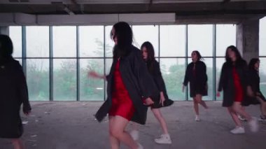 Bir grup dansçı geniş pencereli endüstriyel tarzda bir odada gösteri yapıyorlar. Kırmızı kıyafetlerin üzerine siyah ceketler giyiyorlar, senkronize hareketler sergiliyorlar. Atmosfer enerjik ve dinamik..