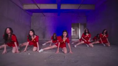 Kırmızı elbiseli bir grup dansçı boş ve endüstriyel bir alanda senkronize bir gösteri yapıyorlar. Aydınlatma mor aksanlarla loş, dramatik bir atmosfer yaratıyor..