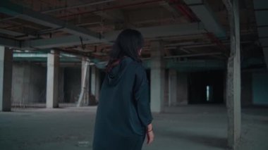 Terk edilmiş bir sanayi bölgesinde duran genç bir kadın düşünceli bir şekilde uzaklığa bakıyor. Kurulumda beton sütunlar ve loş ışıklı bir atmosfer yer alıyor, yalnızlık ve yansıma hissi yaratıyor..