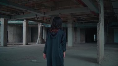 Genç bir kadın terk edilmiş bir sanayi bölgesinde duruyor ve derin bir ifadeyle başka yere bakıyor. Onun uzun saçı yavaşça akar ve koyu renk büyük bir ceket giyer. Arka planda beton sütunlar ve loş bir atmosfer yer alıyor.
