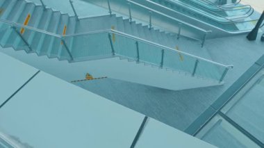 Camdan parmaklıkları ve parlak bir tasarımı olan, duvarında uyarı işareti olan modern bir merdiven. Merdivenler aydınlık ve çağdaş mimari düzenlerle çevrili..