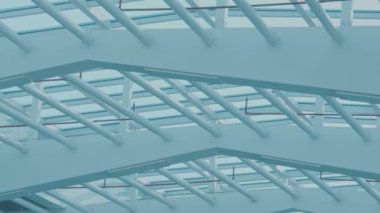 Kesişen kirişler ve cam panellerden oluşan modern bir mimari yapı, açık mavi gökyüzüne karşı geometrik desen oluşturuyor..