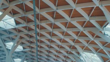 Tahta levhalar ve beyaz kirişlerle geometrik bir tasarımı olan modern bir mimari tavan. Yapıda doğal ve endüstriyel maddelerin bir karışımı açık ve havadar bir atmosfer yaratıyor..