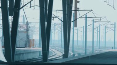 Uzağa uzanan zarif mimari destekleri ve rayları olan modern bir tren istasyonu platformu. Sahne bir ışık sisi içinde, sakin bir atmosfer yaratıyor..